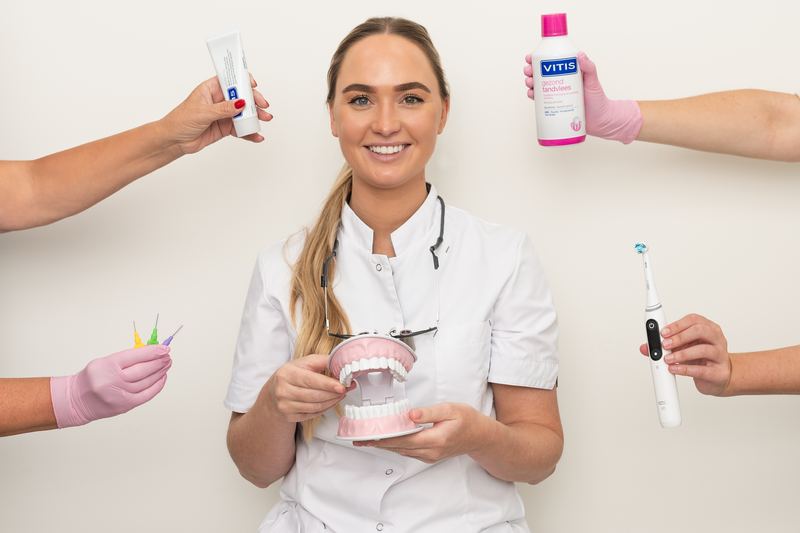 Mondhygiënist met gebitsmodel, omringd door tandpasta, mondspoeling, ragers en een elektrische tandenborstel